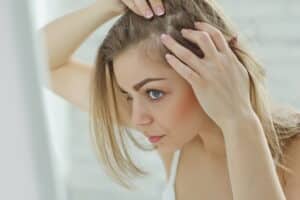 A woman looking at her thinning hair in the mirror, considering NeoGraft for women