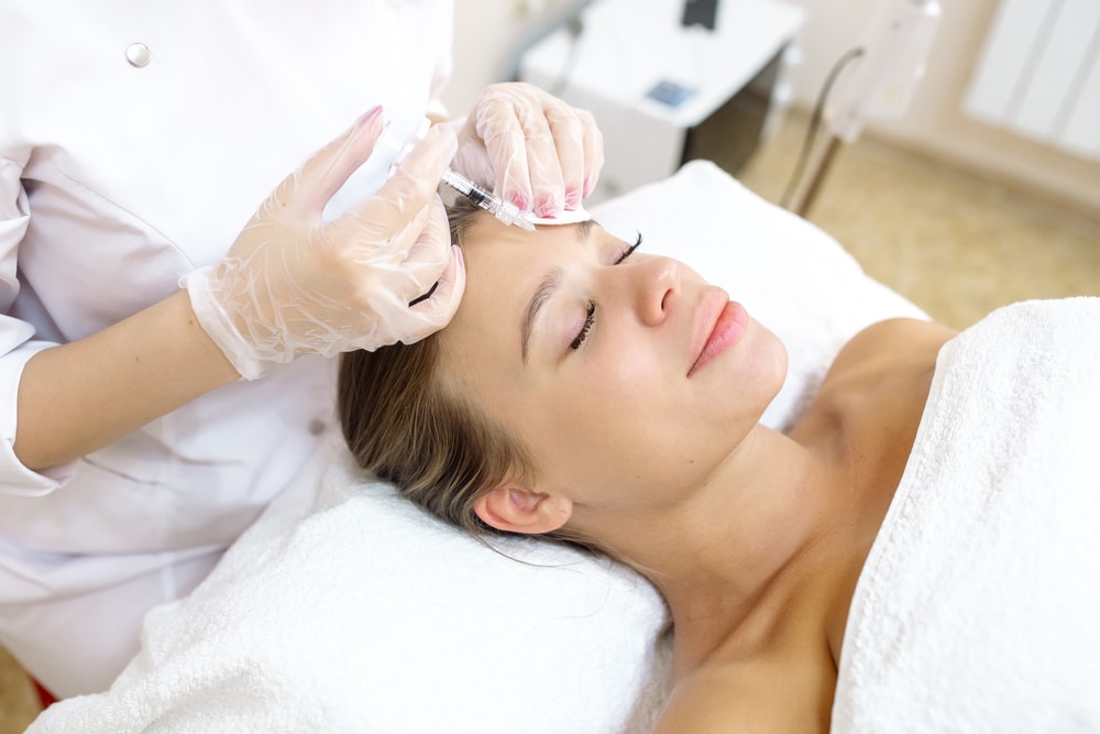 Beautiful woman in her 30s receives a Xeomin injection to smooth frown lines between her brows for a rejuvenated appearance.