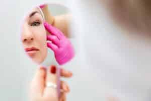 Woman looking at her face in a hand mirror after receiving Ultherapy treatment for tighter, firmer skin.